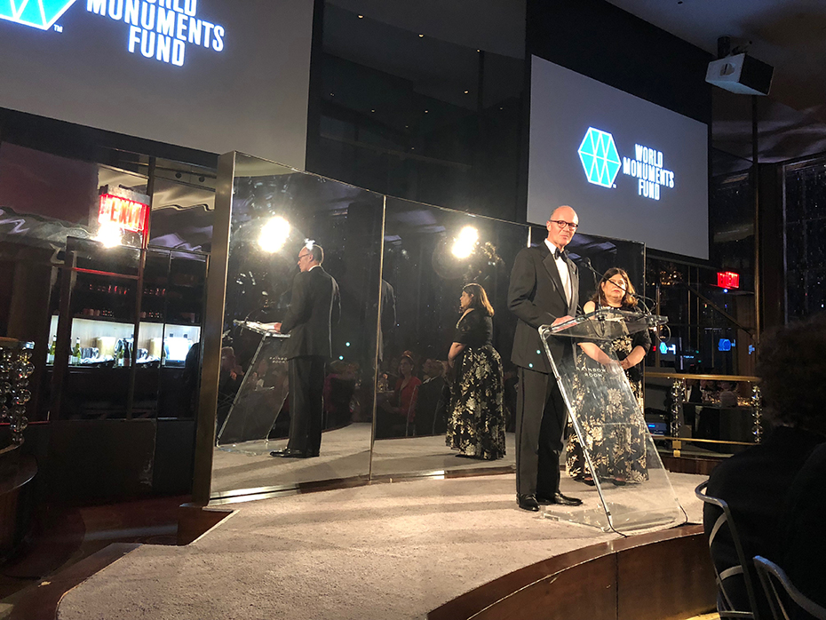 A man on stage in front of a three sided mirror at the World Monuments Fund’s 2018 Hadrian Gala