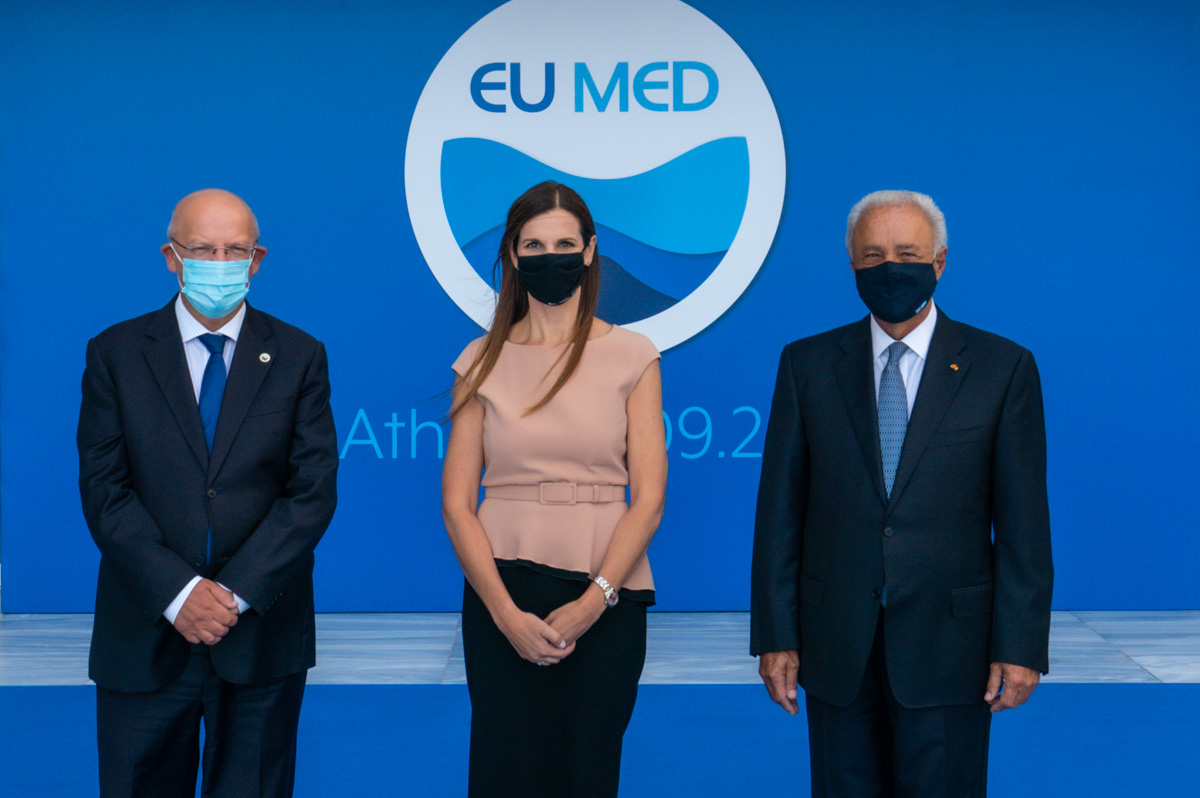 Two men and a woman between them are photographed in front of the EU MED background