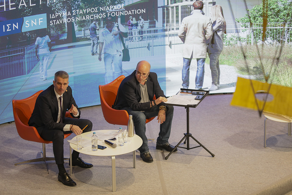 Andreas Drakopoulos, President of the Stavros Niarchos Foundation sits with another man on stage