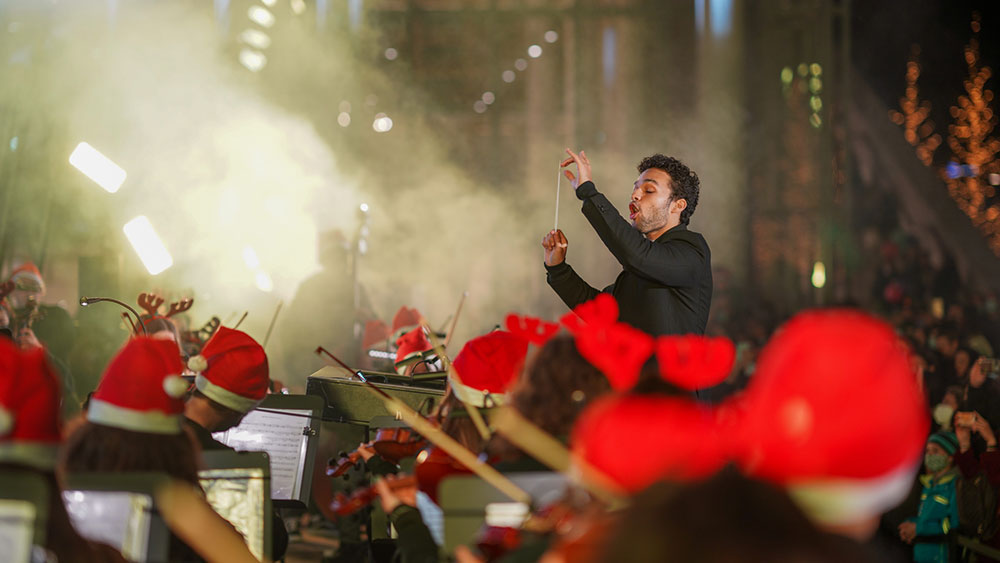 A man conducts an orchestra with Christmas hats at the Stavros Niarchos Foundation Cultural Center