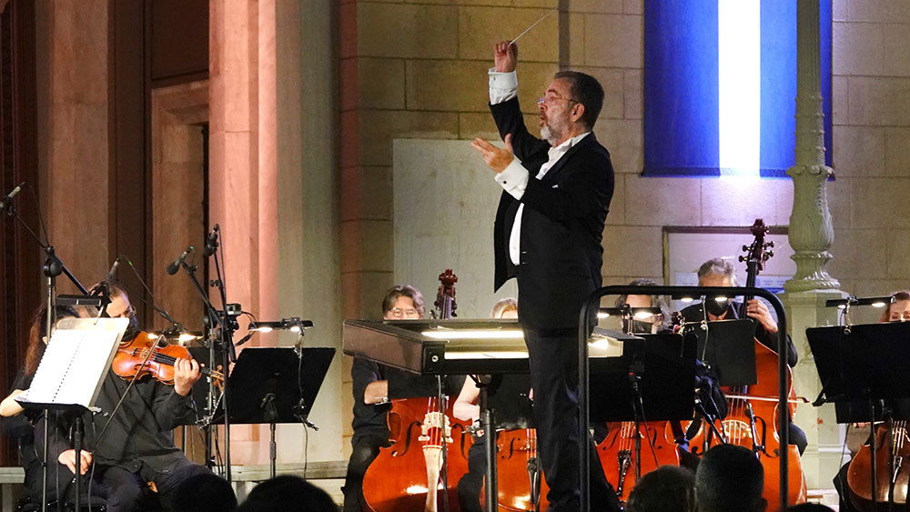 A conductor in the center of the stage directs the members of the orchestra who are seated with their instruments
