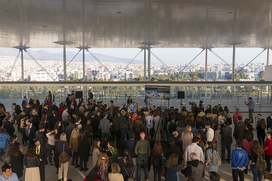 Distant photo showing a crowd of people standing and watching a speech