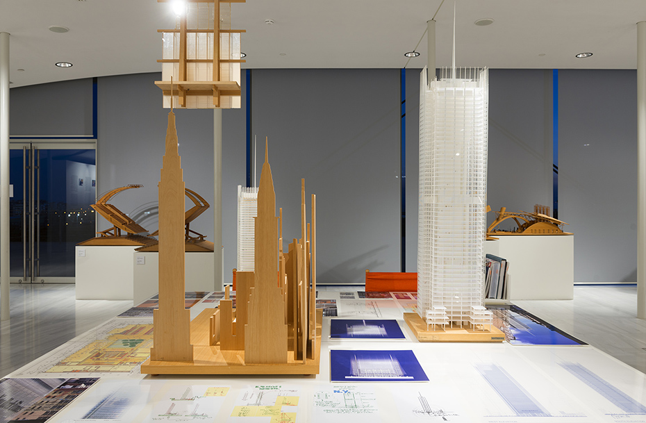 Two models showing tall buildings placed on a table with the accompanying drawings and notes around them