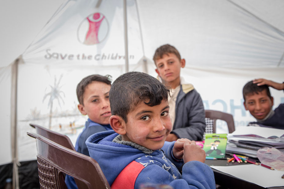 Four young boys sitting around a table drawing and posing for a photo