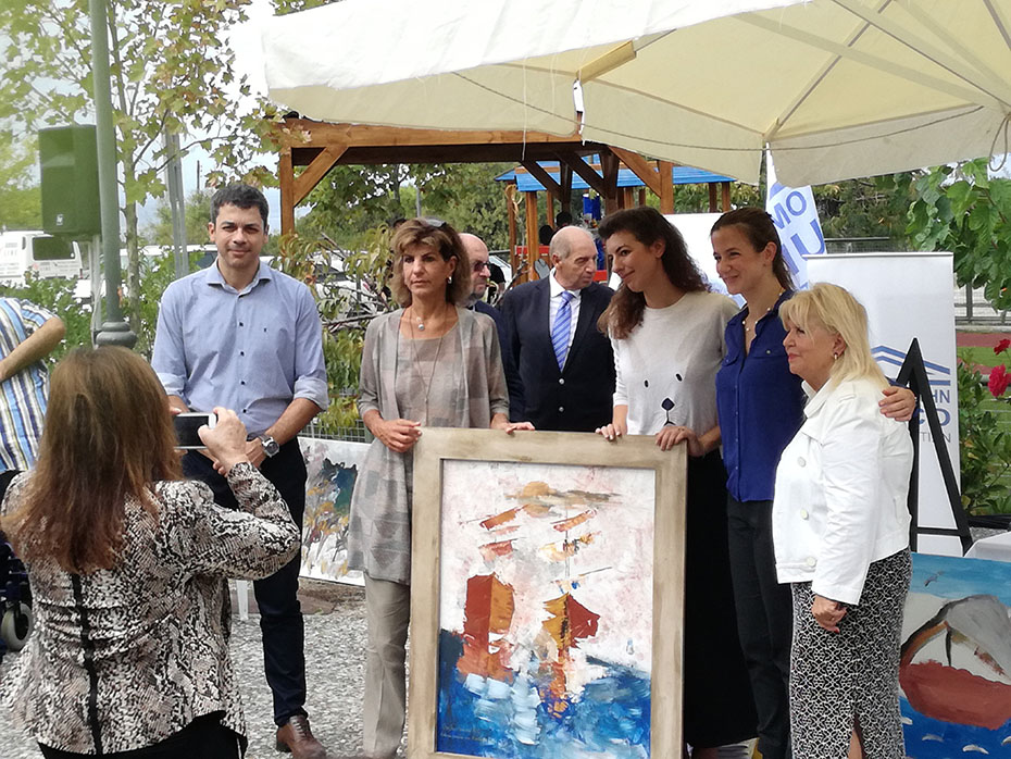 A woman takes a picture of members of the Stavros Niarchos Foundation and the Rehabilitation Center for Disabled Children of Attica, who hold a painting