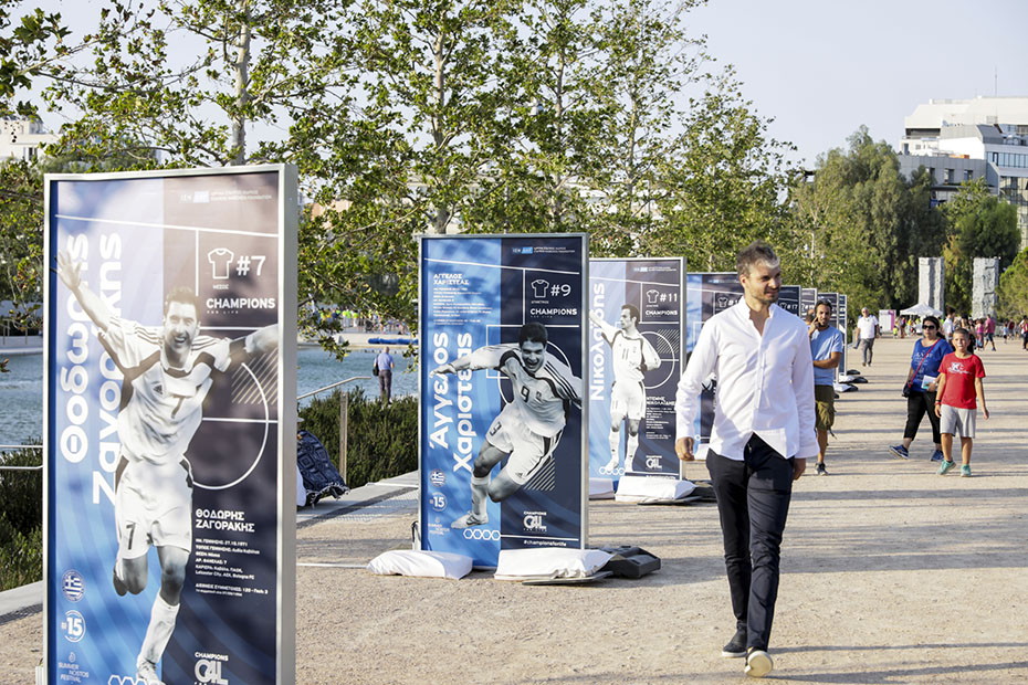 Ένας άντρας περπατάει δίπλα από τα banners που δείχνουν έναν ένα τους παίκτες την ελληνικής ποδοσφαιρικής ομάδας