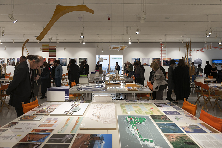 Photo showing a crowd of people walking by and looking at tables on which there are drawings, memos and mock-ups