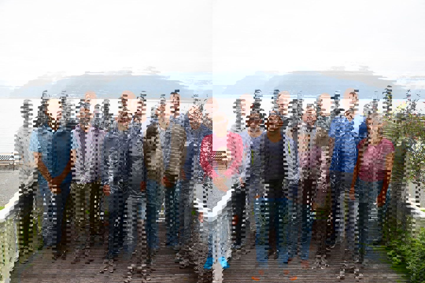 Μια ομάδα ανθρώπων στέκεται σε ένα ξύλινο ντεκ μπροστά από τη θάλασσα για μια φωτογραφία.