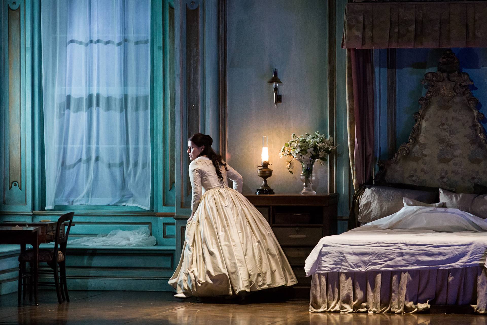A woman wearing a gown looks anxiously outside her window at her chamber.