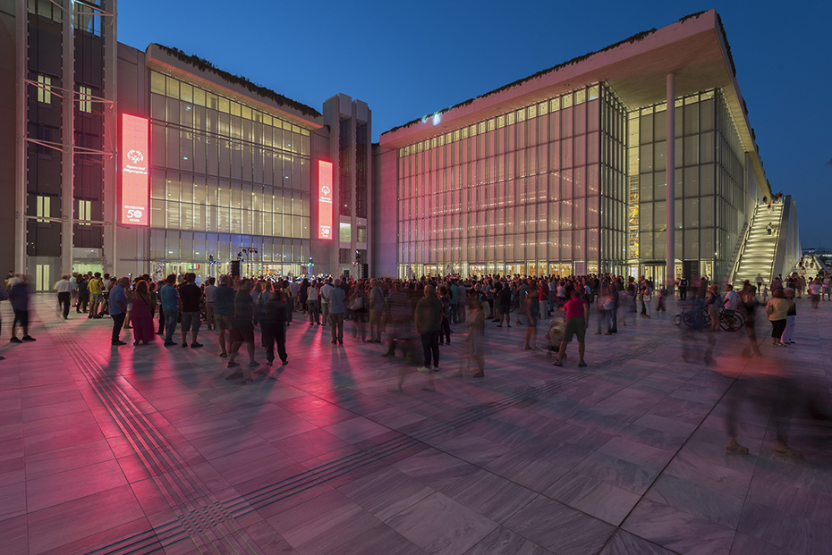 Photo showing a crowd of people standing between the outdoor space created by two glass buildings