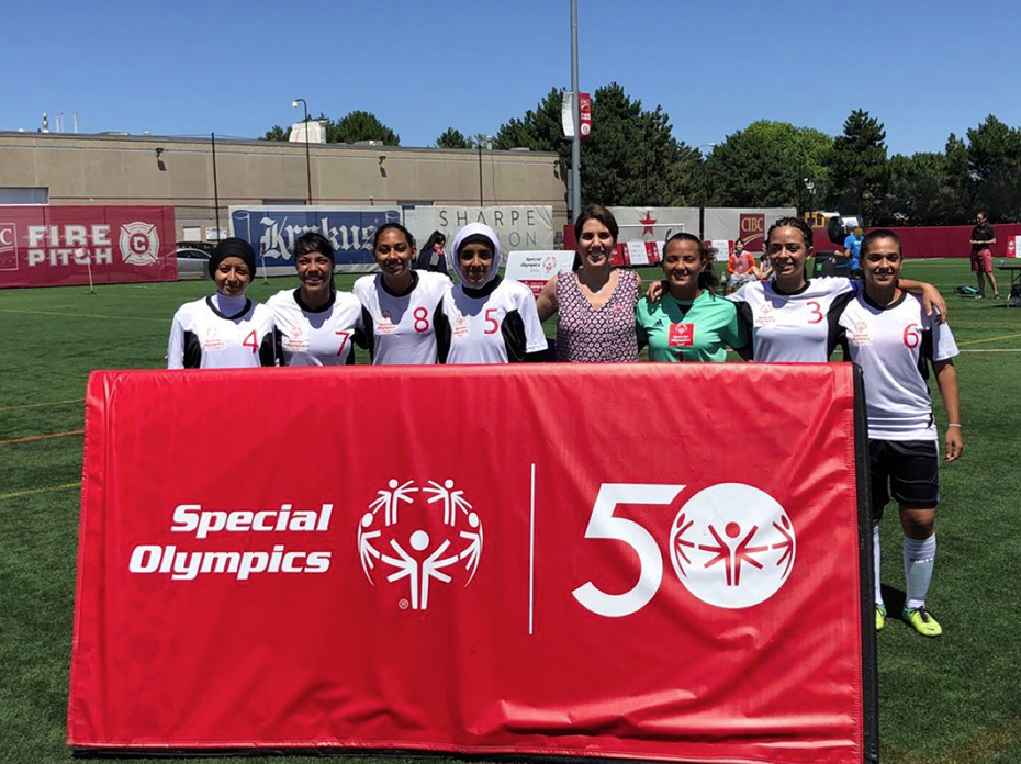 A group of women dressed in the same football uniform hold a banner that reads Special Olympics 50 years and are photographed on the field