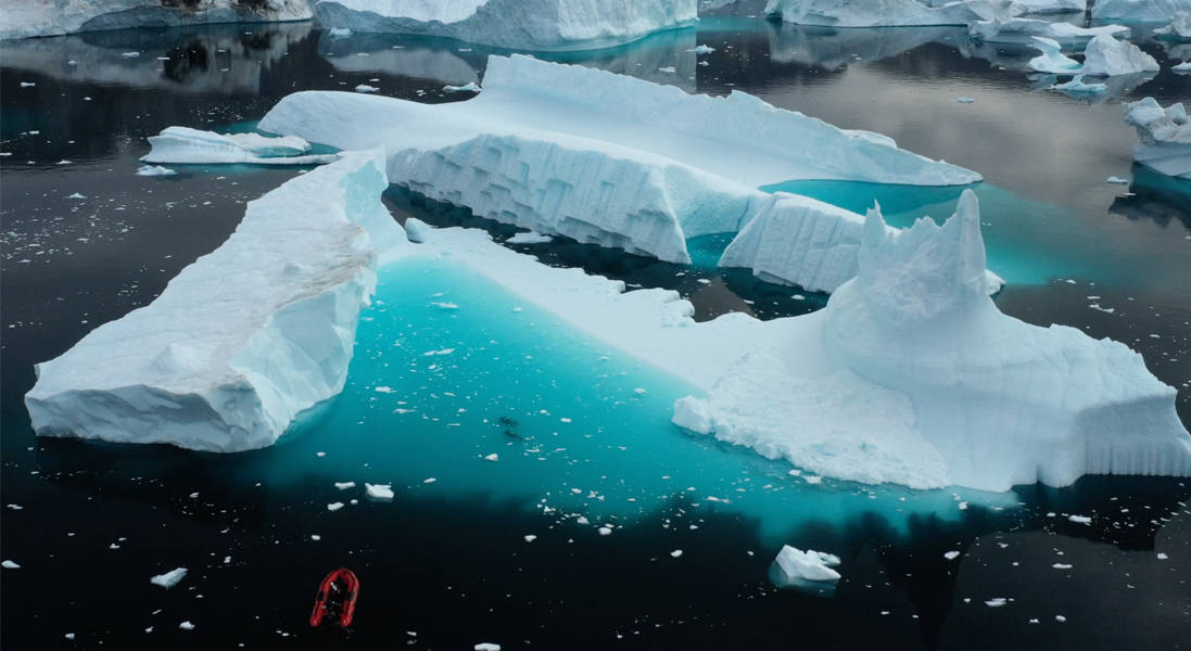 Δύο δύτες επισκιάζονται από το παγόβουνο δίπλα στο οποίο κολυμπούν.