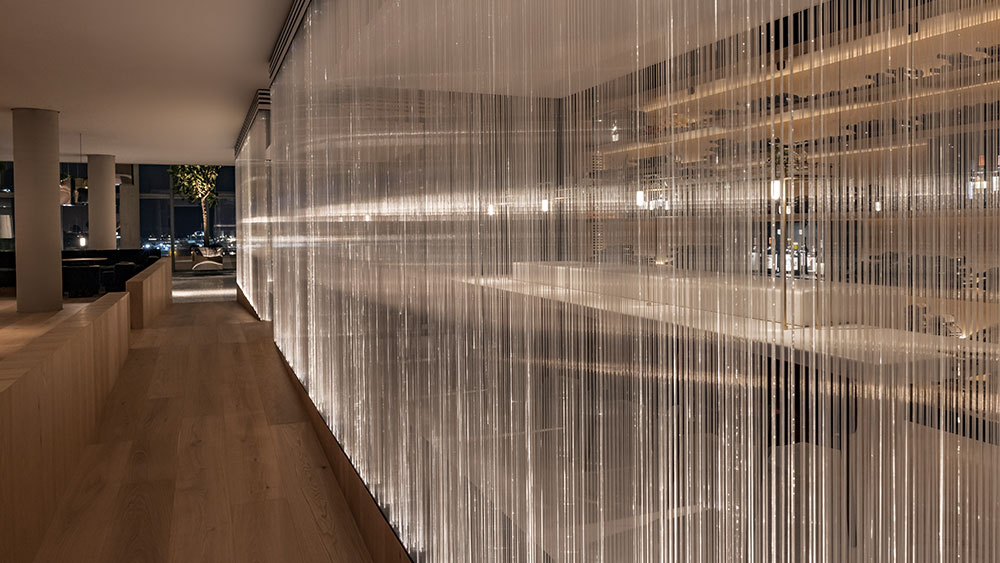 In the interior of a restaurant there is a transparent partition curtain made of threads of light