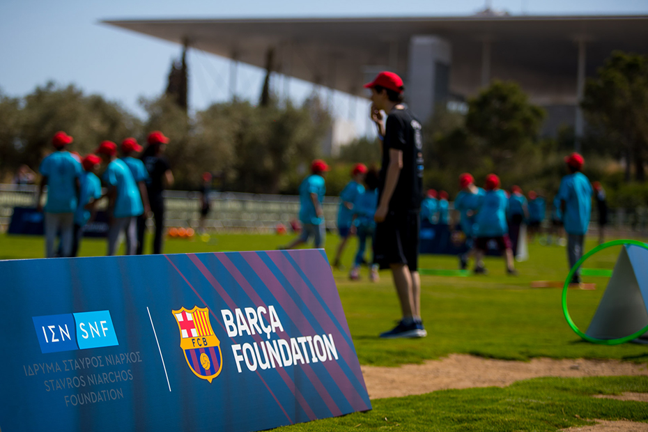 Children playing on a soccer field, with Barca Foundation stands surrounding the field