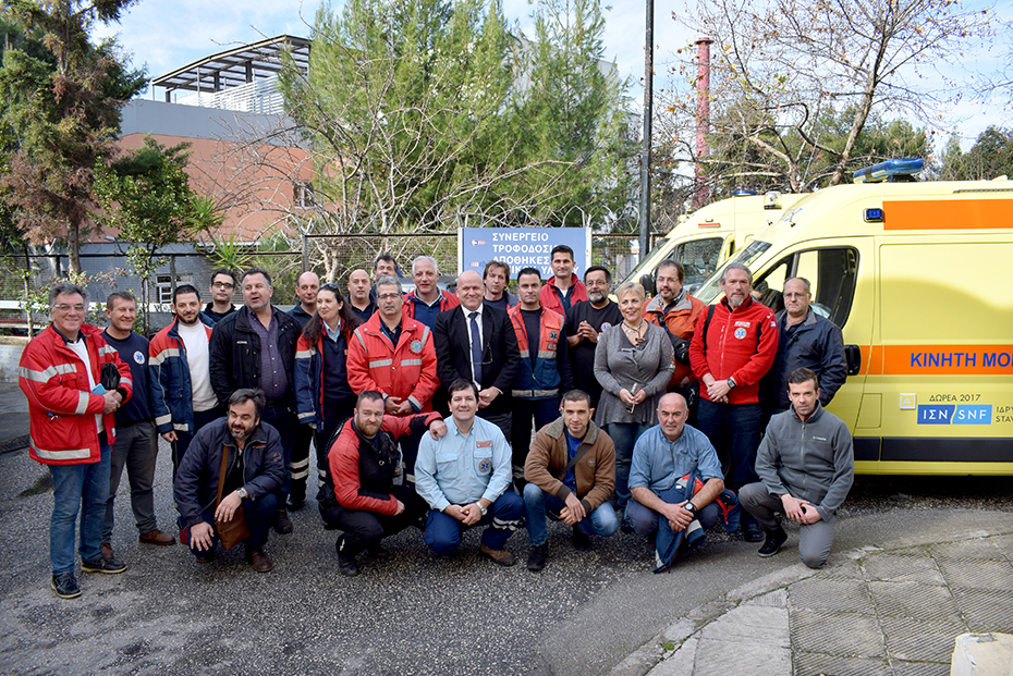 A group of EKAV crew members stand for a picture with members of the Stavros Niarchos Foundation, in front of a few ambulances