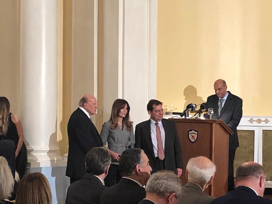 Anna-Kynthia Bousdoukou stands between two men in front of a seated crowd after receiving the Giorgos Karayiannis Journalism and Technology Award