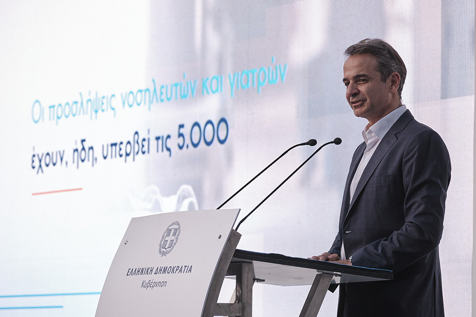 Ο Κυριάκος Μητσοτάκης, Πρωθυπουργός της Ελλάδας, στέκεται στο βήμα και μιλάει ενώ δίπλα του προβάλλεται η φράση