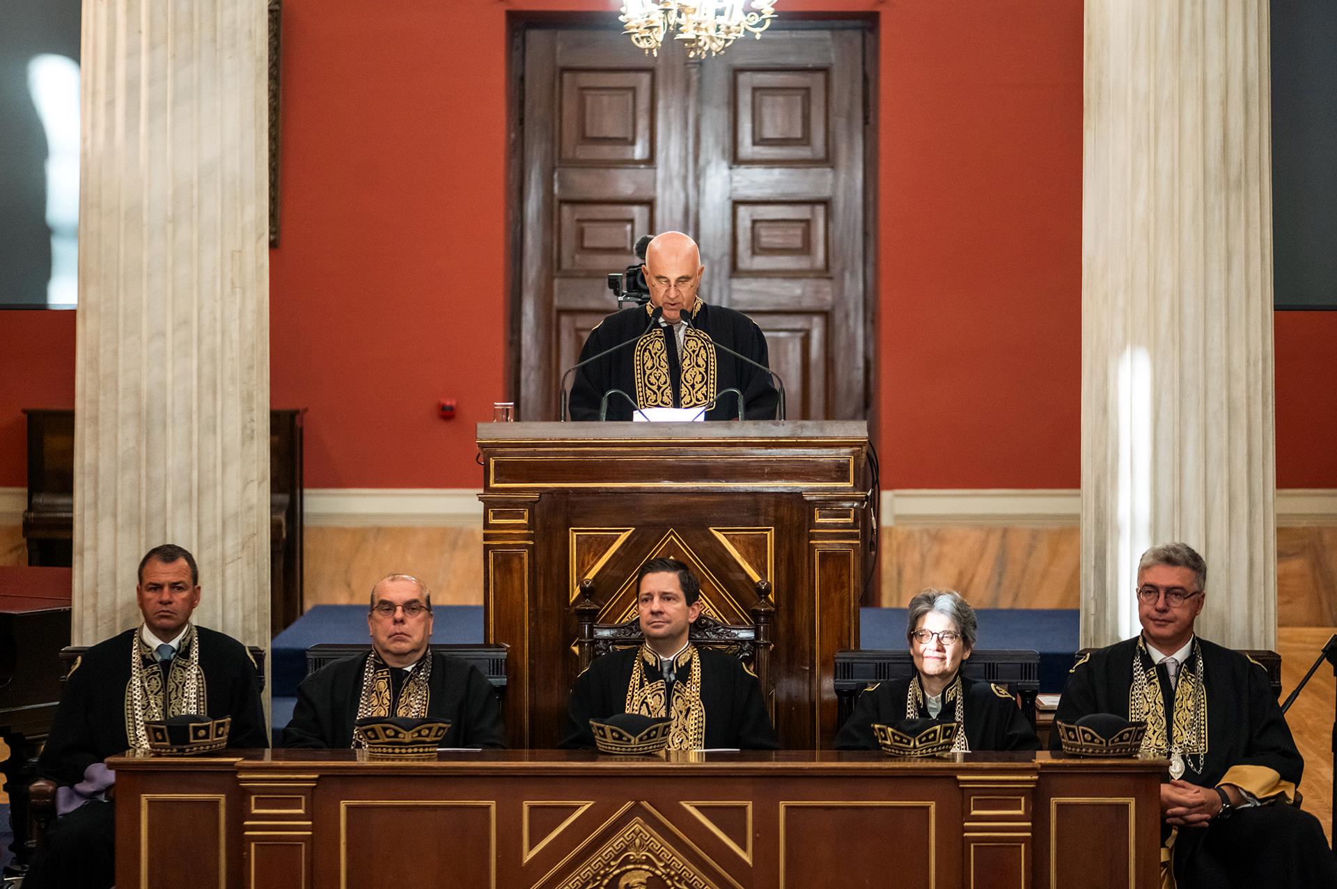 Professor Pavlos Miriantheus standing at the podium, dressed in a gown, during the reading of the official resolution to confer the title of doctor honoris causa of the Departments of Medicine and Nursing.