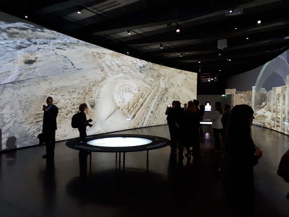 In a room with huge cinema screens, people see what some cities looked like in ancient times