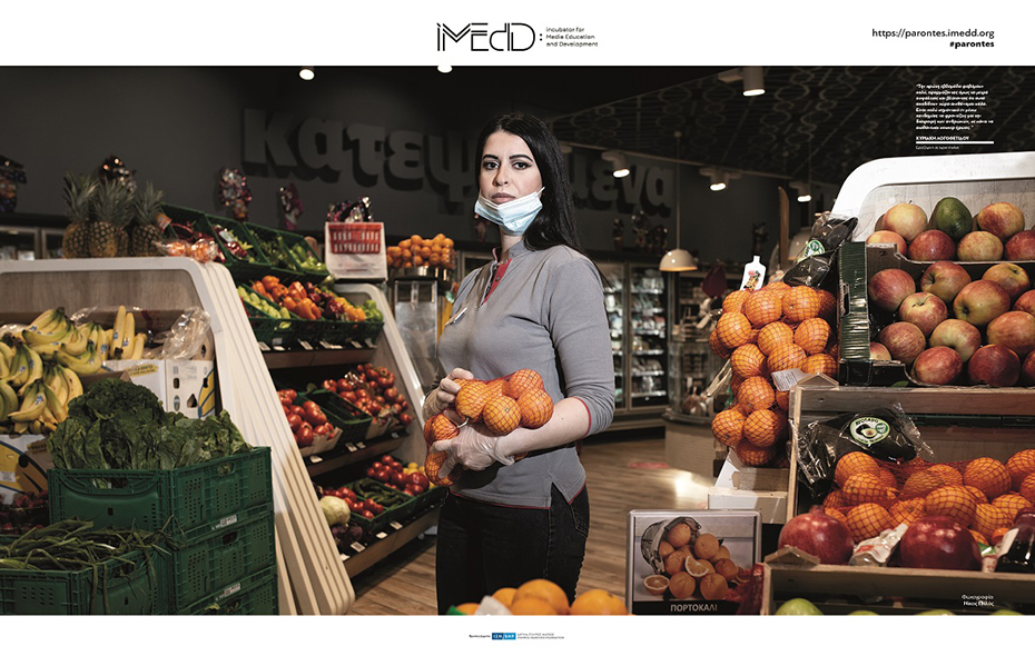 Photo showing a woman working in the fruits and vegetables department of a supermarket holding oranges in her arms