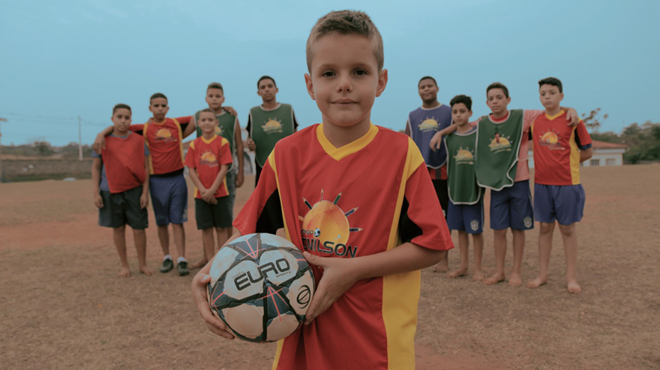 A little boy is holding a soccer ball and the rest of the team is standing behind him with their arms around him