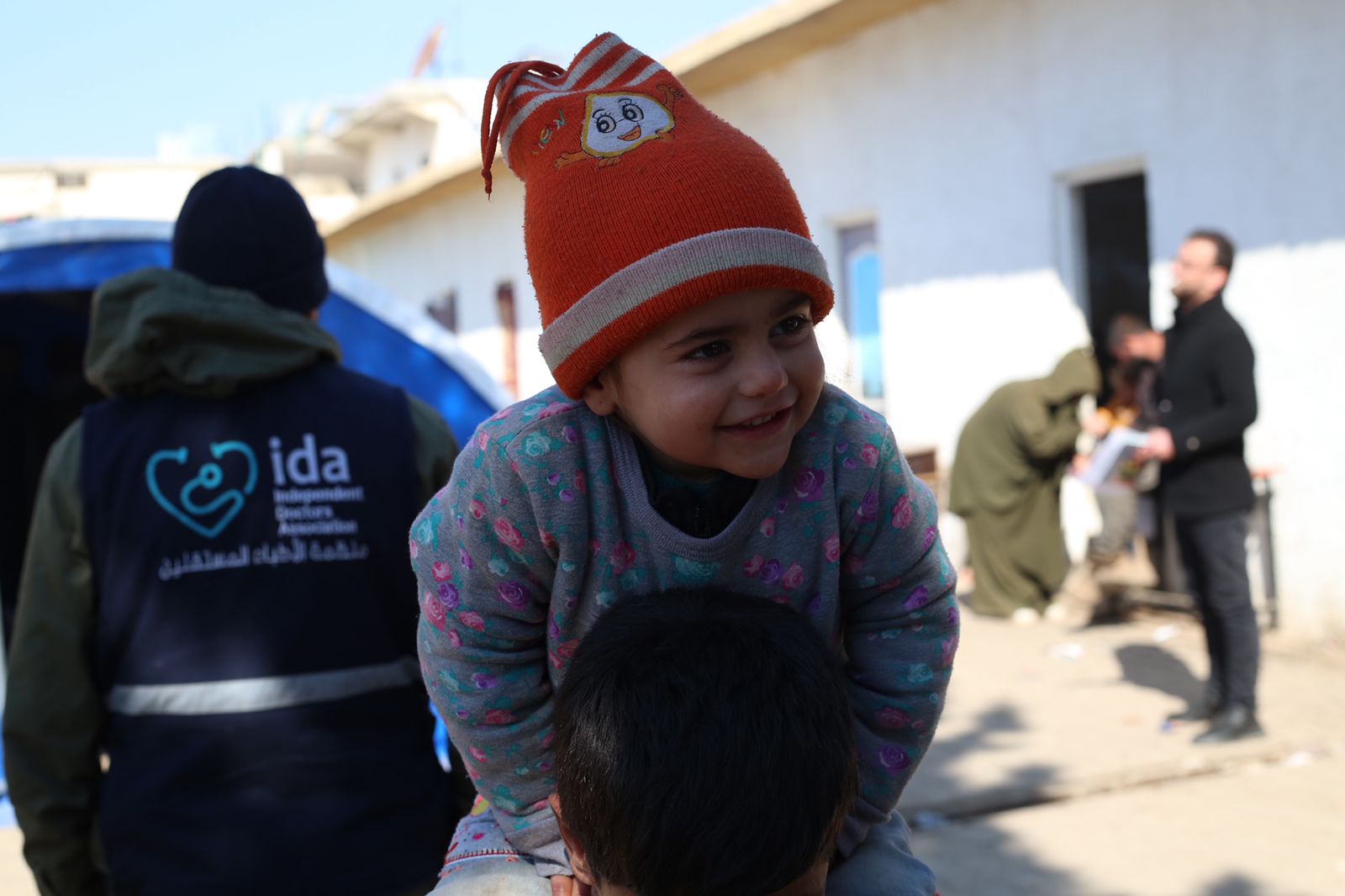 A child smiles near an adult in an Independent Doctors Association vest.