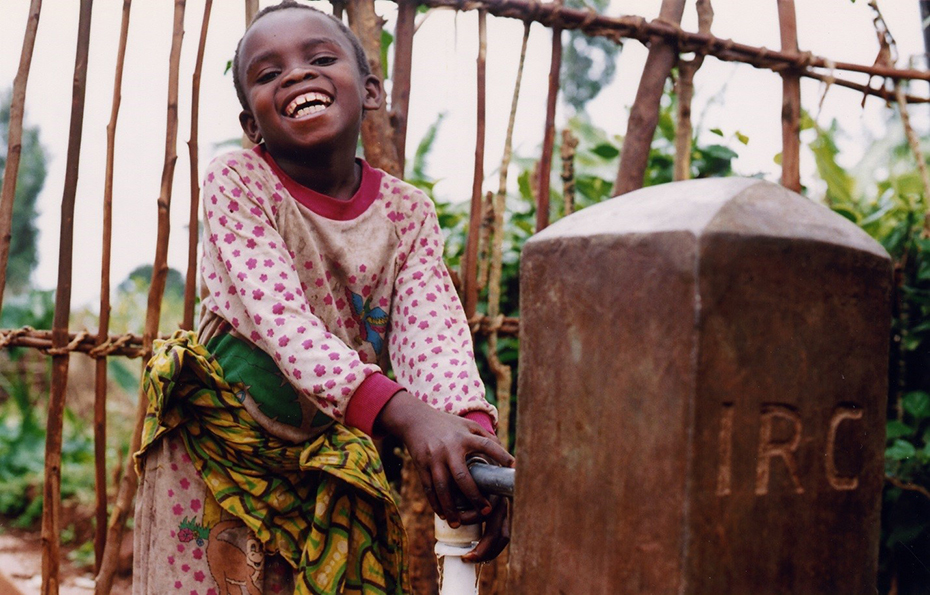 A little girl smiles and uses a water tap