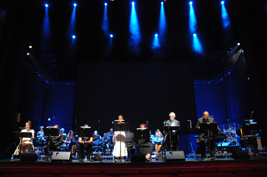 Seven people sing on stage in front of a choir
