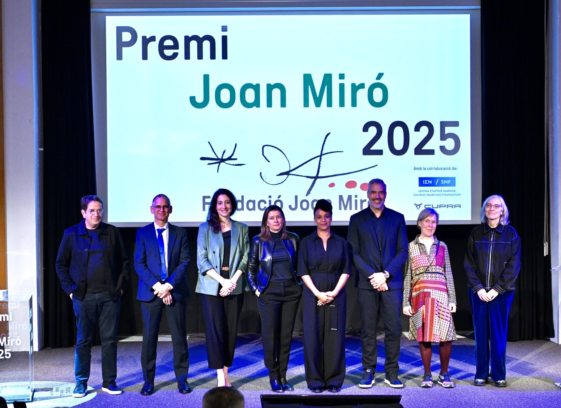 A group of people on the stage pose for a photo and there is a screen behind them dispaying Fundació Joan Miró signage and the logos of the Stavros Niarchos Foundation and Cupra.
