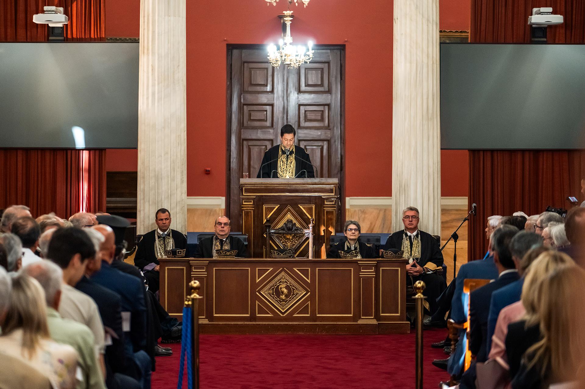 The Rector of the NKUA, Professor Gerasimos Siasos, stands at the podium, dressed in the gown, as he delivers a speech.
