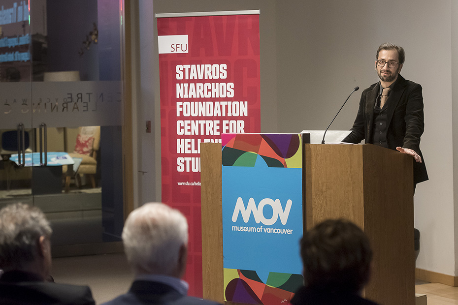 A man on a podium speaks to a seated crowd at the Museum of Vancouver