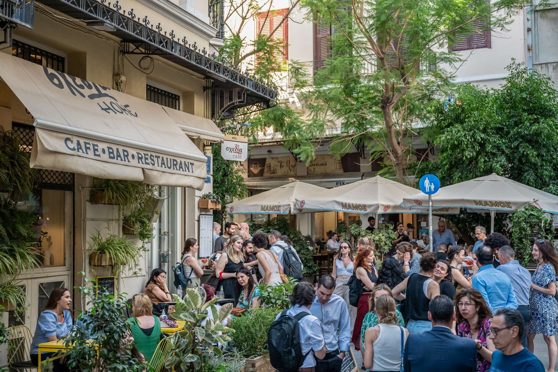Ομάδα ανθρώπων στέκεται έξω από εστιατόριο της πόλης, κουβεντιάζοντας και απολαμβάνοντας την αστική ατμόσφαιρα.