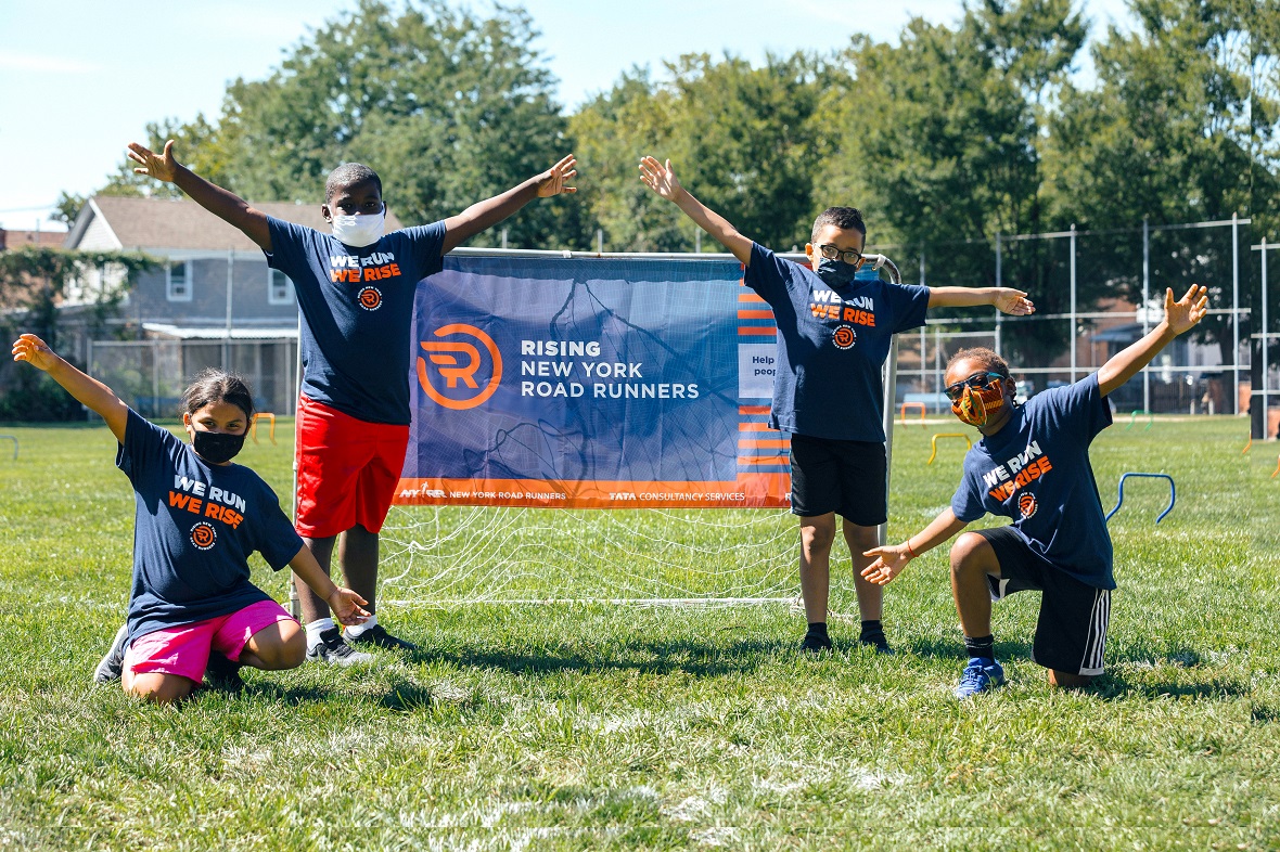 A group of four people on a football field pose with their hands up next to a goal that reads