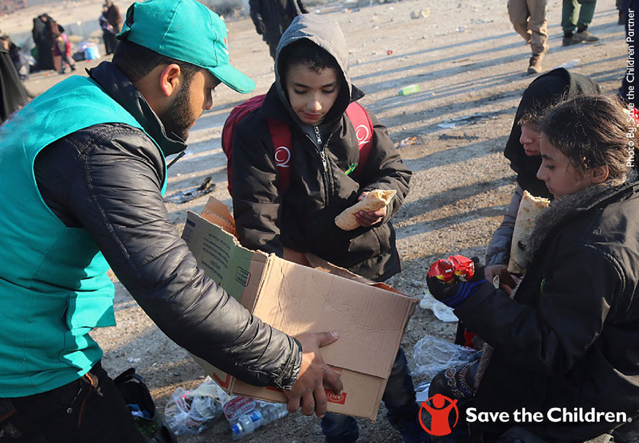 A man holds a box in his hands and offers some of the things in the box to young children