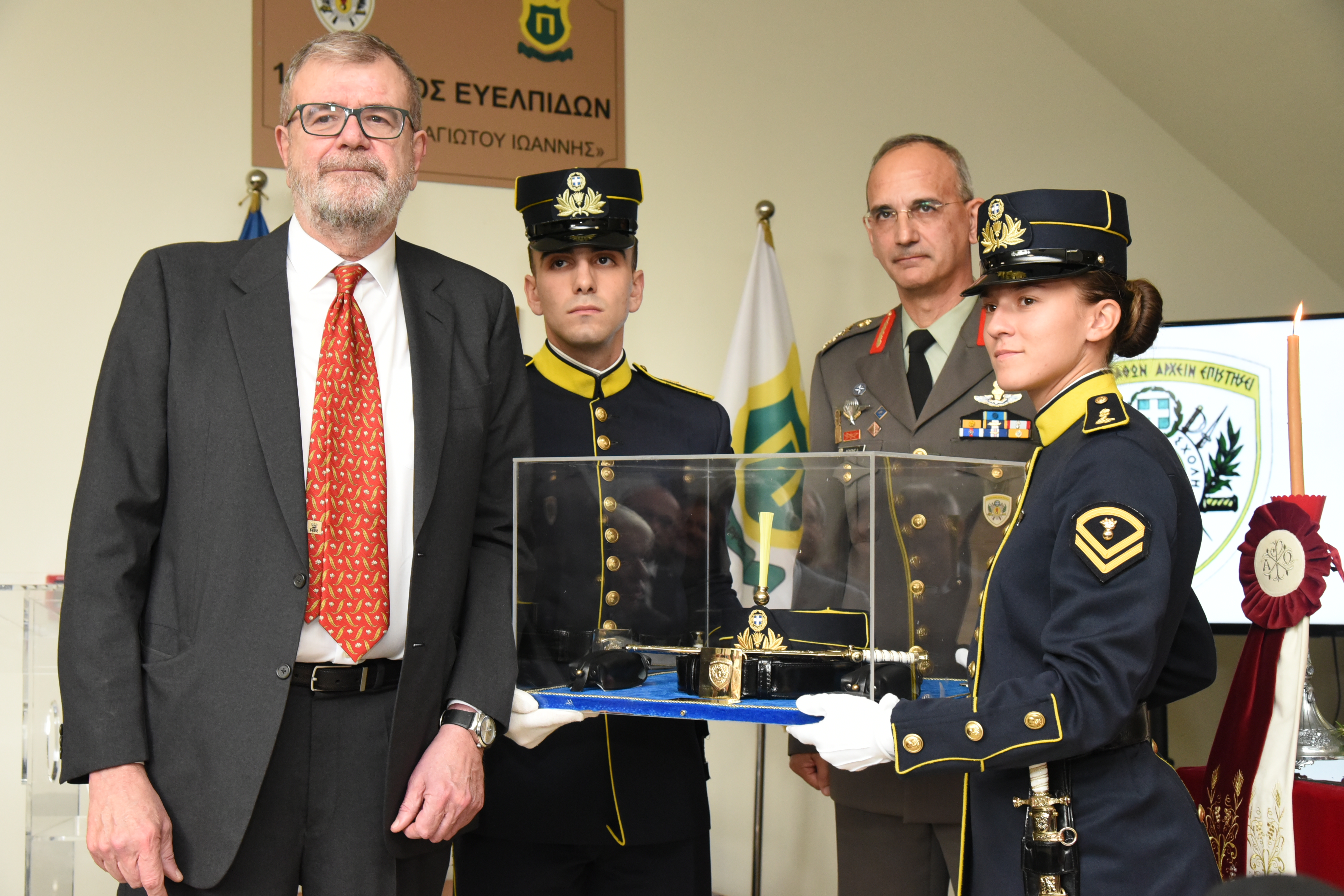 A man stands in front of a young man and woman in army attire, who are holding up an object encased in glass