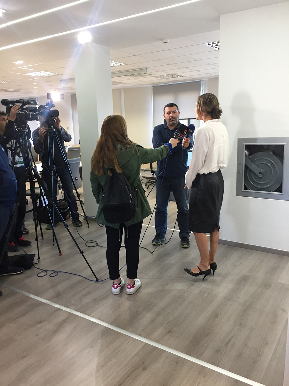 A woman speaks into microphones held by two people and is being filmed by cameramen