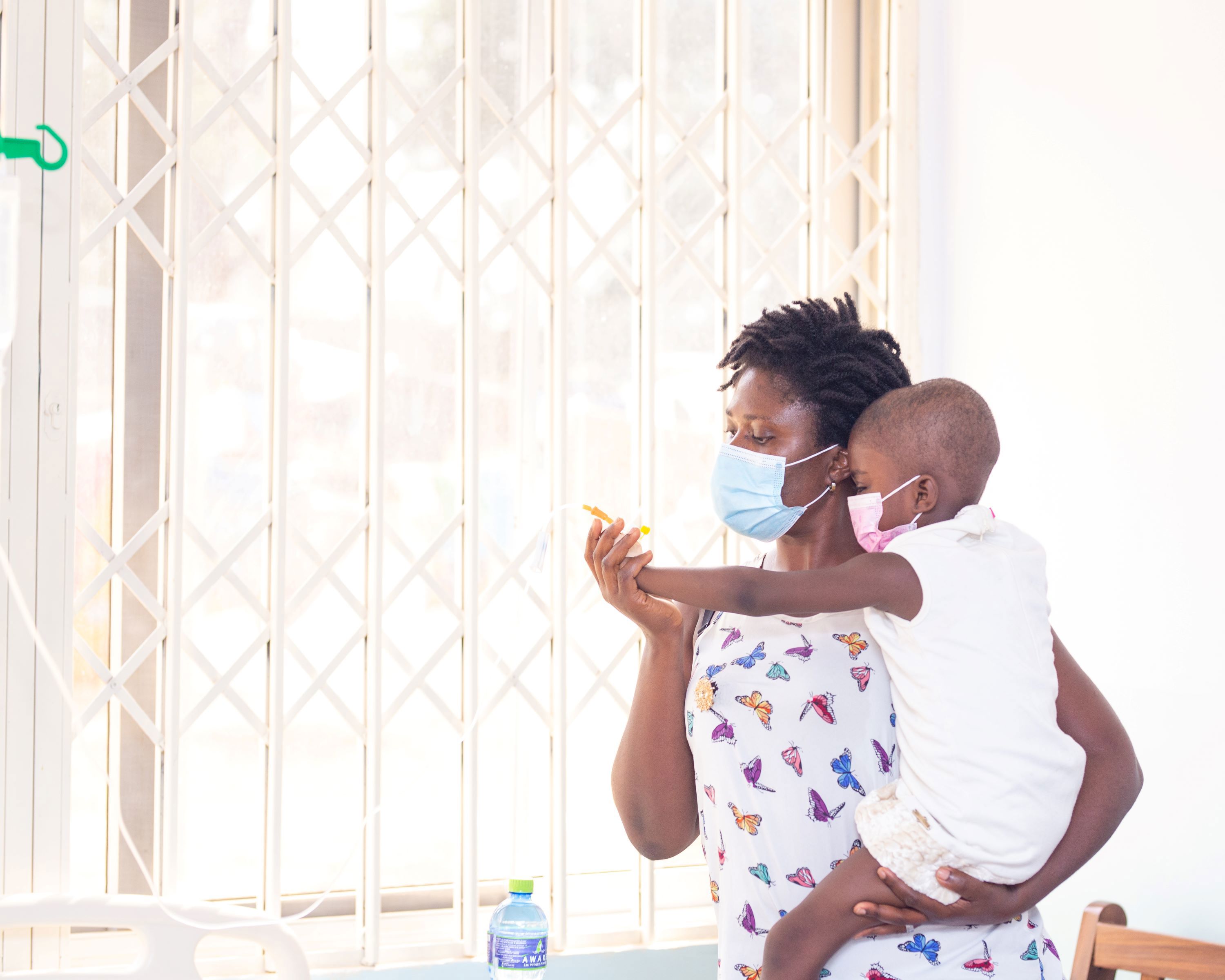 A woman holding a child, both wearing protective face masks