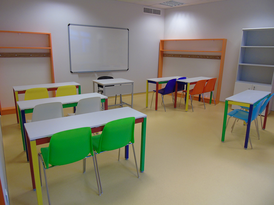 Φωτογραφία από μια μικρή σχολική αίθουσα με έναν λευκό πίνακα και θρανία με πολύχρωμες καρέκλες