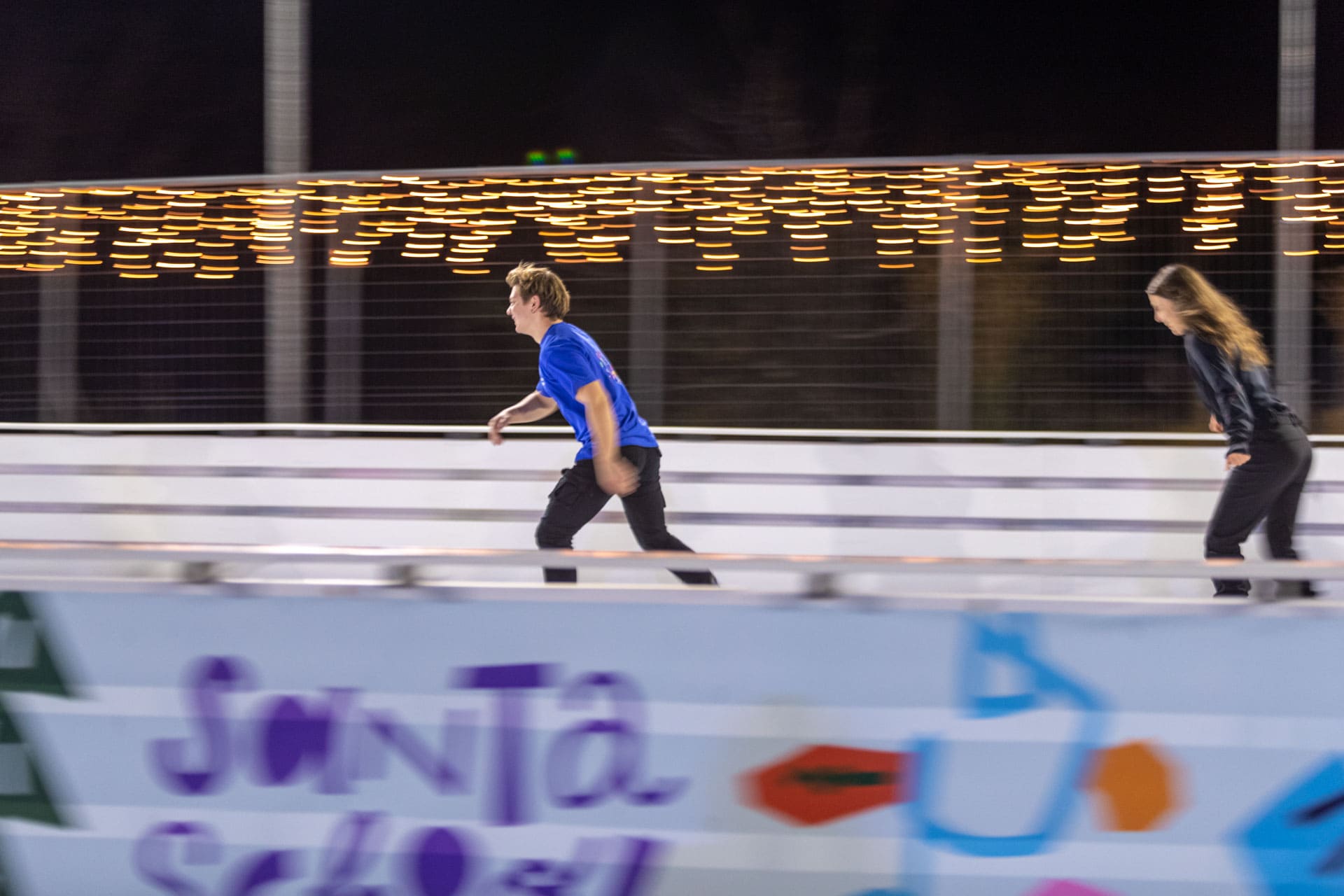 Two people skate in a ice rink.