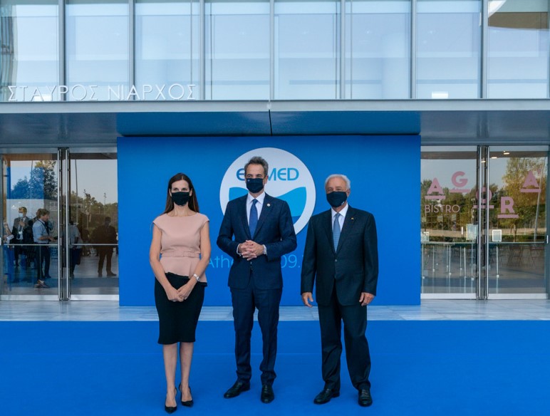 Prime Minister Kyriakos Mitsotakis together with a woman and a man stand in front of the entrance of the Stavros Niarchos Foundation Cultural Centre where a blue carpet has been laid and are photographed