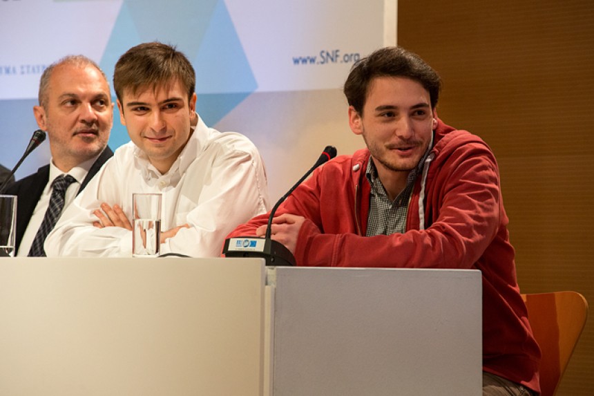 Two young men sit on the conference table on stage at the Stavros Niarchos Foundation Cultural Center