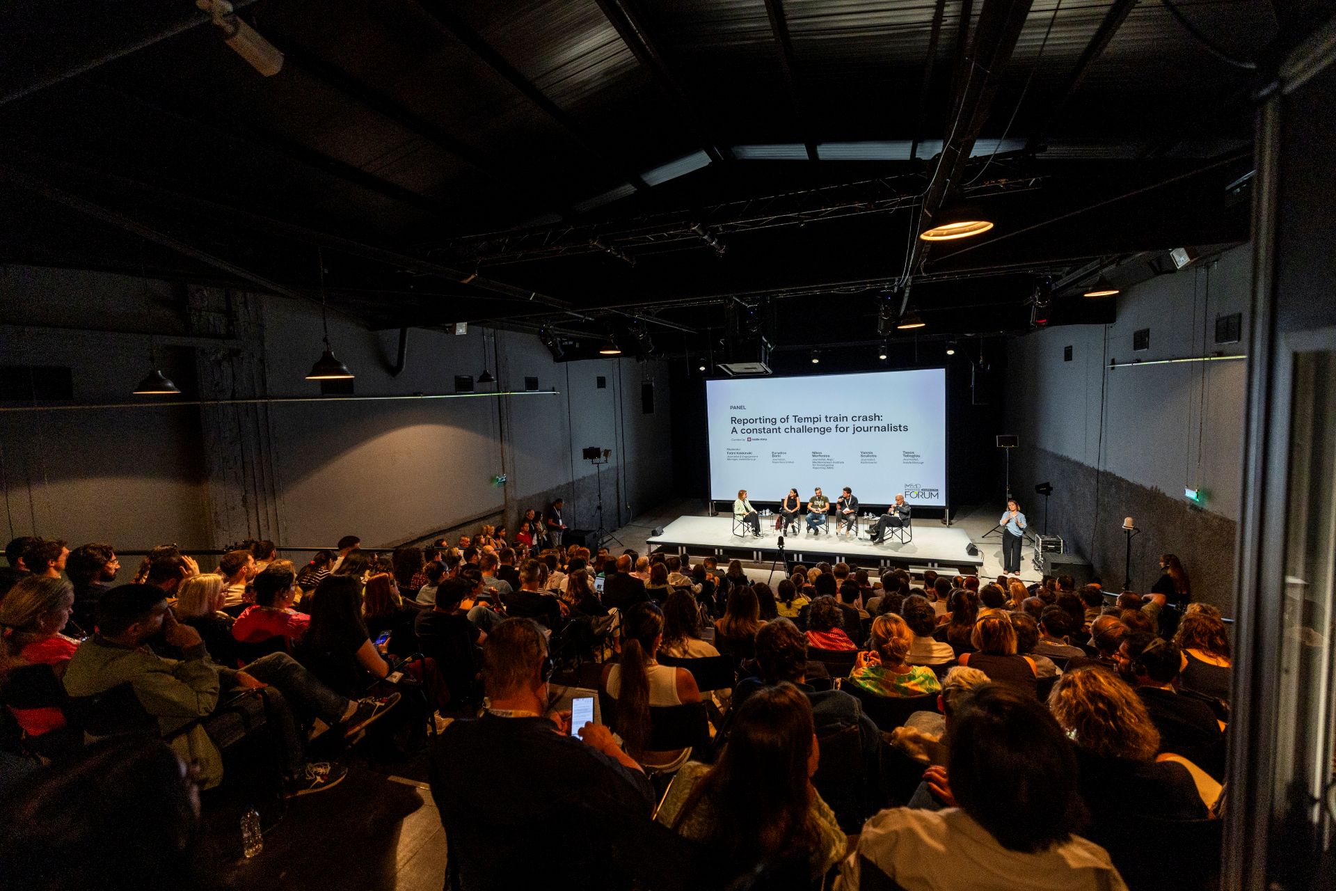 A large audience watches a panel discussion on