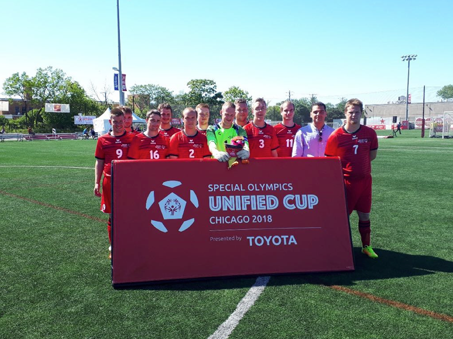 A group of men dressed in the same football uniform hold a banner that reads Special Olympics unified cup Chicago 2018 and are photographed on the field