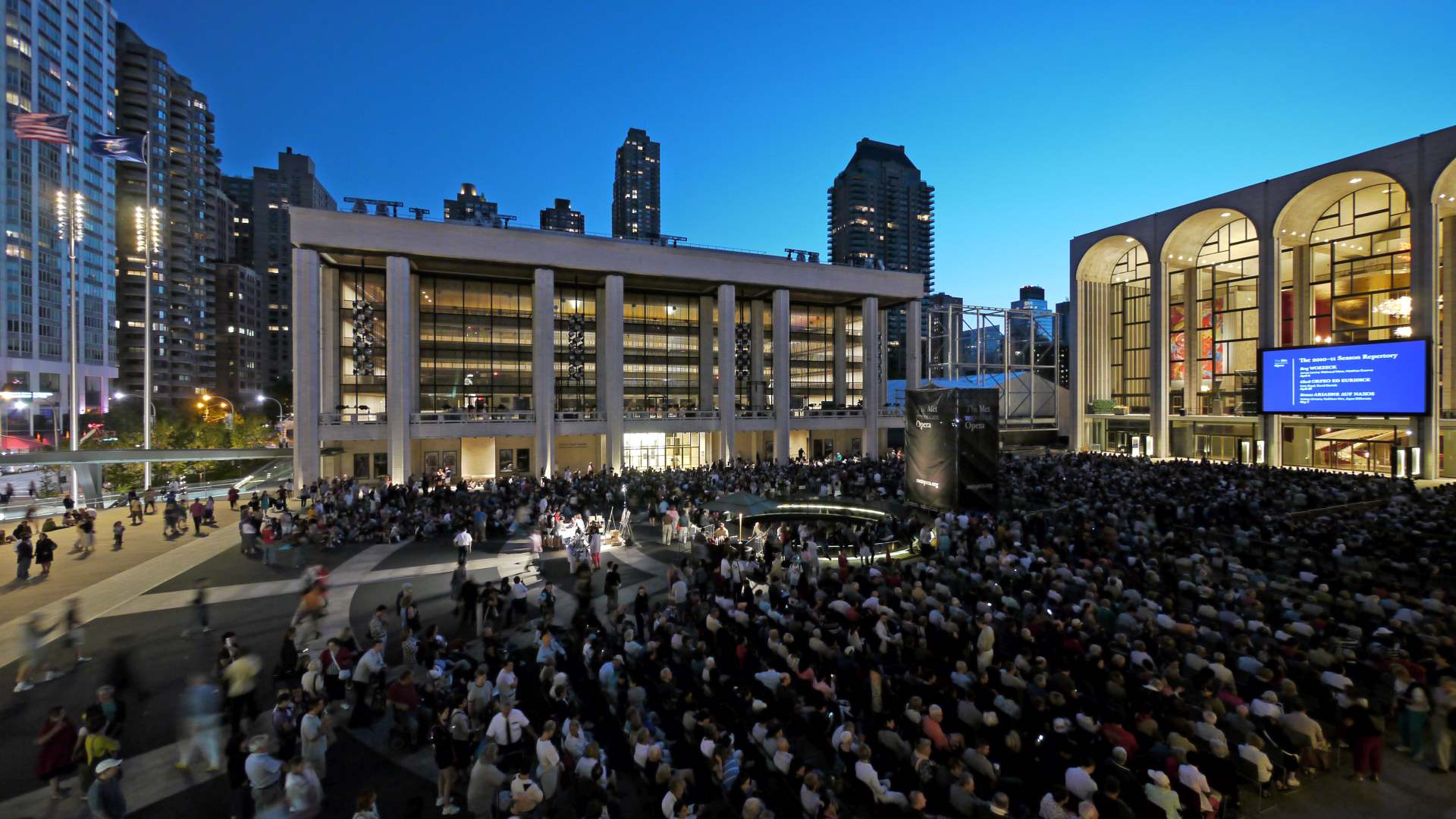 Άνθρωποι συγκεντρωμένοι έξω από το Lincoln Center το σούρουπο, περιτριγυρισμένο από τη λάμψη των φώτων της πόλης.