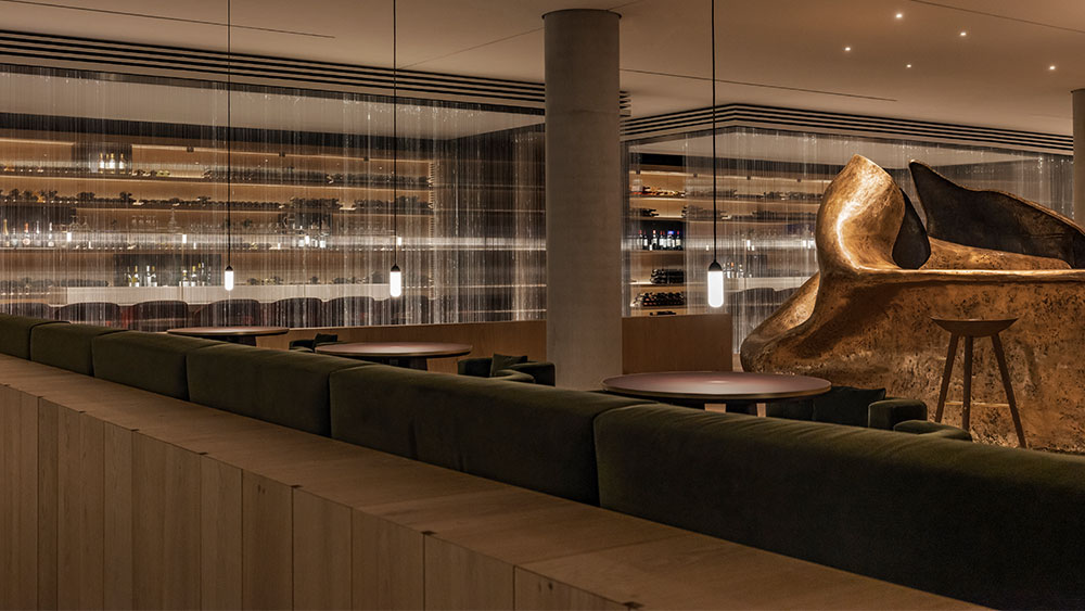 The interior of a restaurant where gold, massive works of art, a transparent curtain of light threads and round tables can be seen