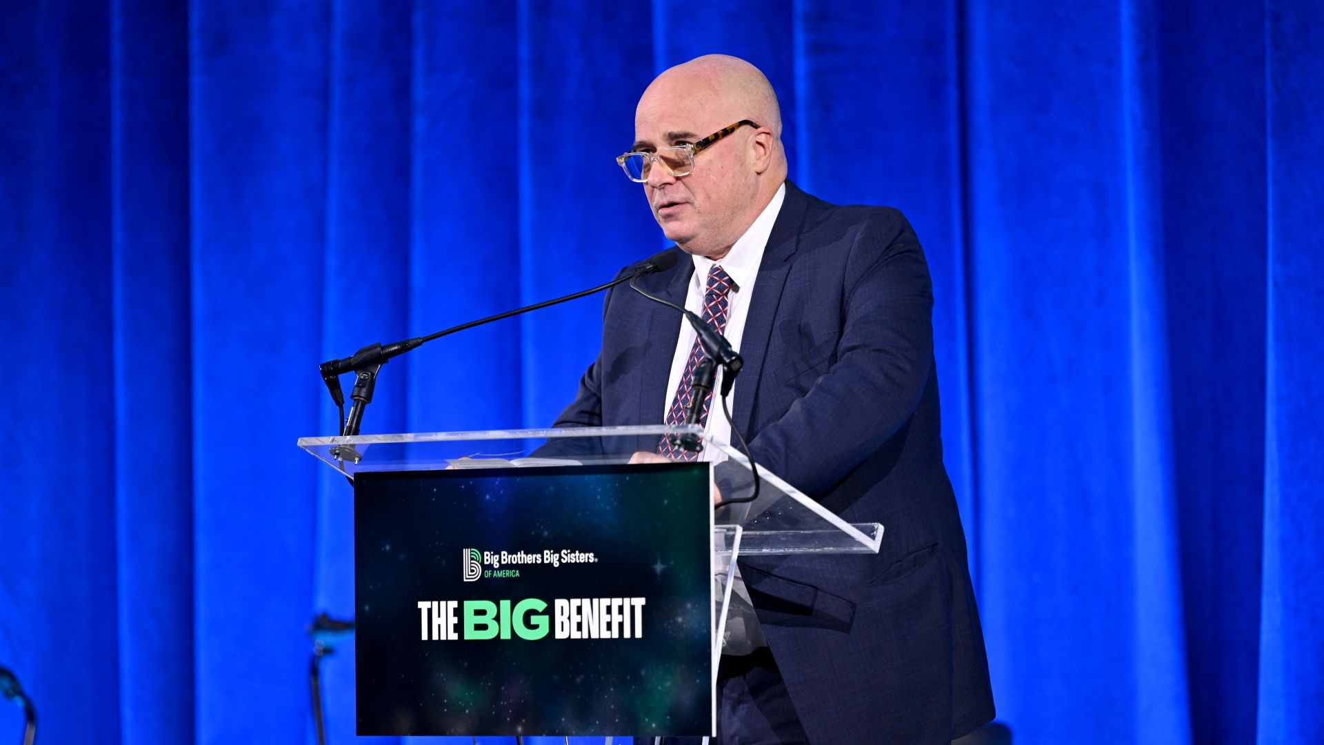 Andreas Dracopoulos, SNF Co-President speaks at a podium in front of a blue curtain.