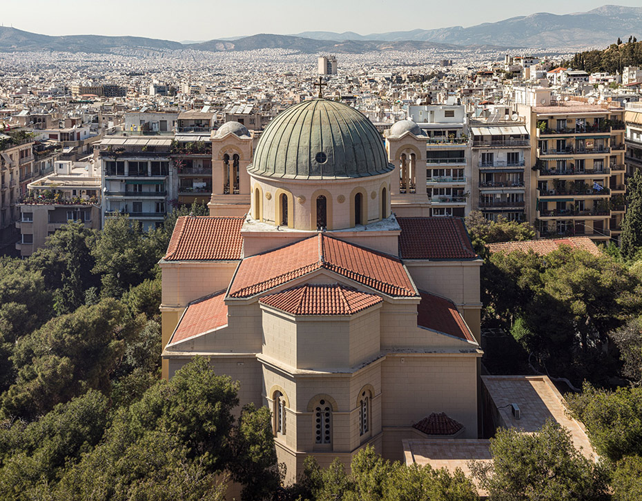 A church in the middle of trees looking onto a distant view of Athens
