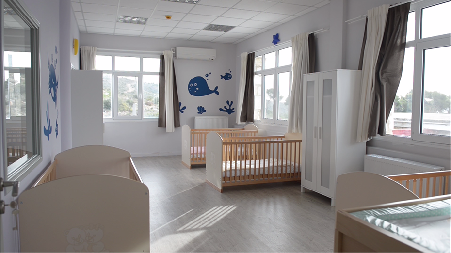 A baby room in which there are baby cribs, white wardrobes and on the walls there are whales and fishes