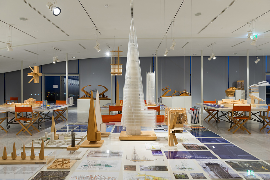 Close-up photo of a table on which there are drawings, notes and models of buildings of different sizes and designs