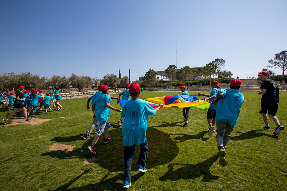 Children hold a colorful sheet and run in a circle in a soccer field